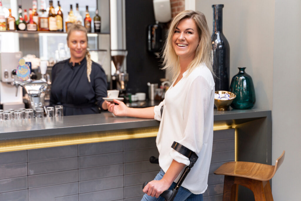 Vrouw met krukken bestelt een koffie aan de bar